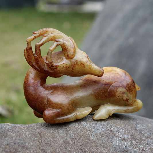 Round-carved sculpture of a lying deer looking back