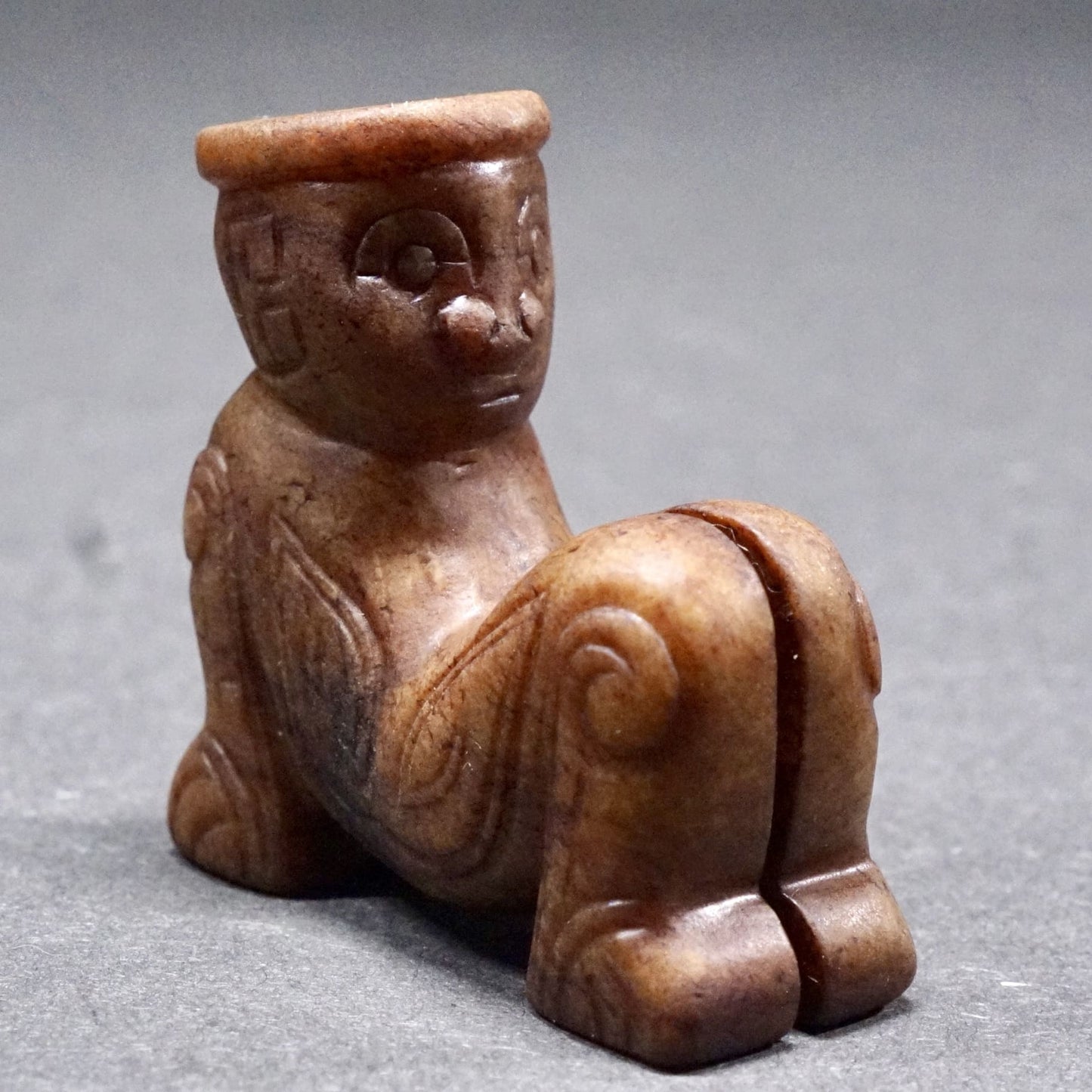 Round sculpture of a jade figure sitting with her arms propped up