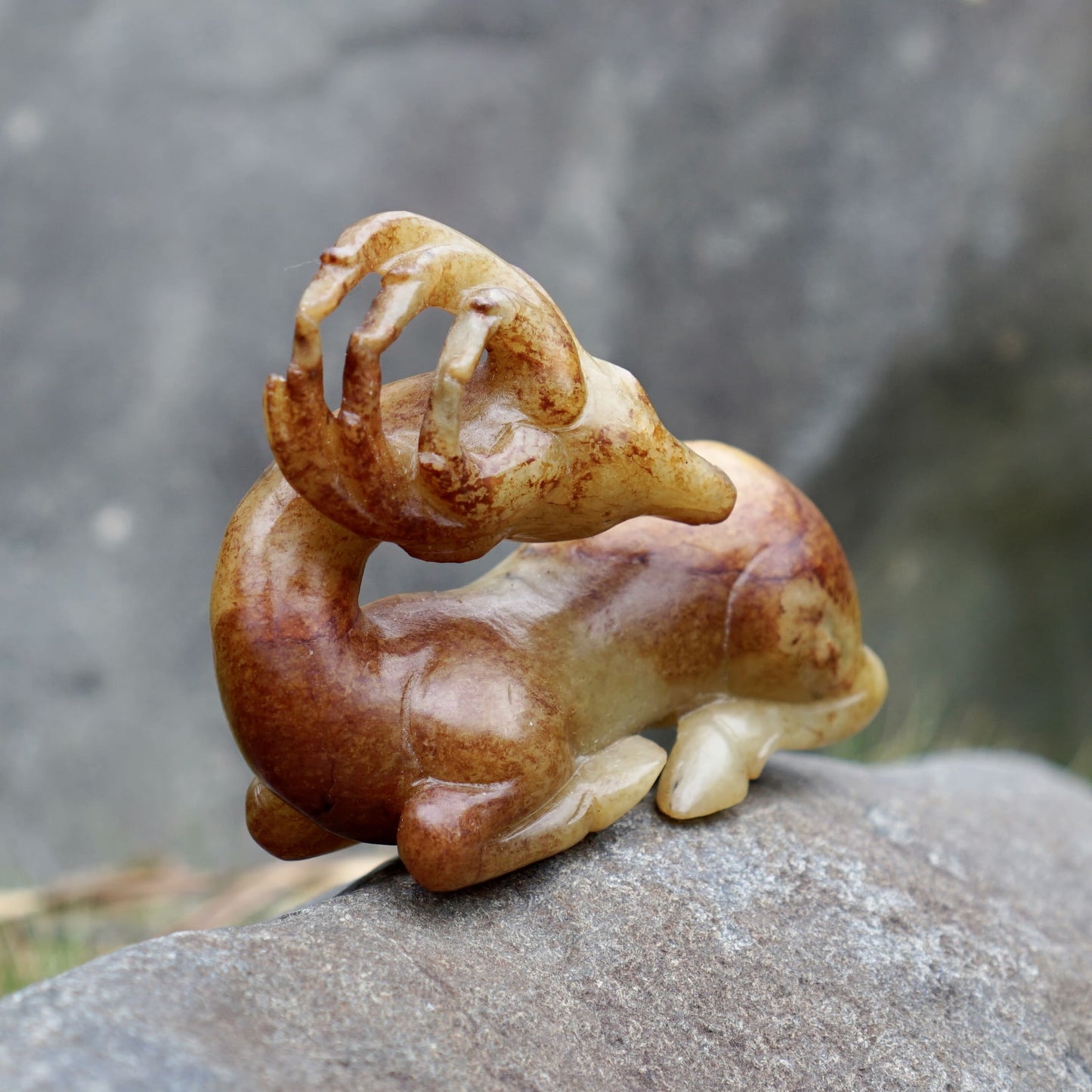 Round-carved sculpture of a lying deer looking back